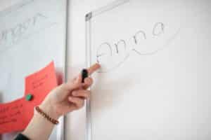 Während der Stottertherapie wird ein Whiteboard verwendet, um Wortsilben darzustellen, ein zeigender Finger erklärt an den Wortsilben das Erlernen des weichen und flüssigen Sprechen zu erlernen.